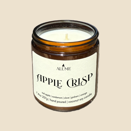 Candle in a glass jar labeled 'Apple Crisp' by Alume on a white background