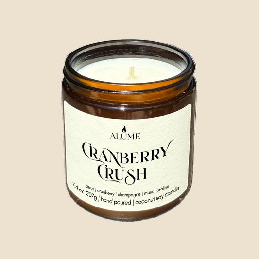 Candle in a glass jar labeled 'Alume Cranberry Crush' on a white background