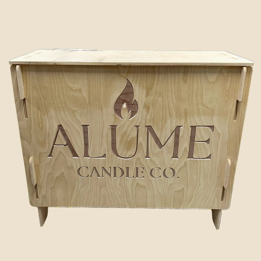 A wooden retail display kiosk with the Alume Candle Co. logo carved into the front.